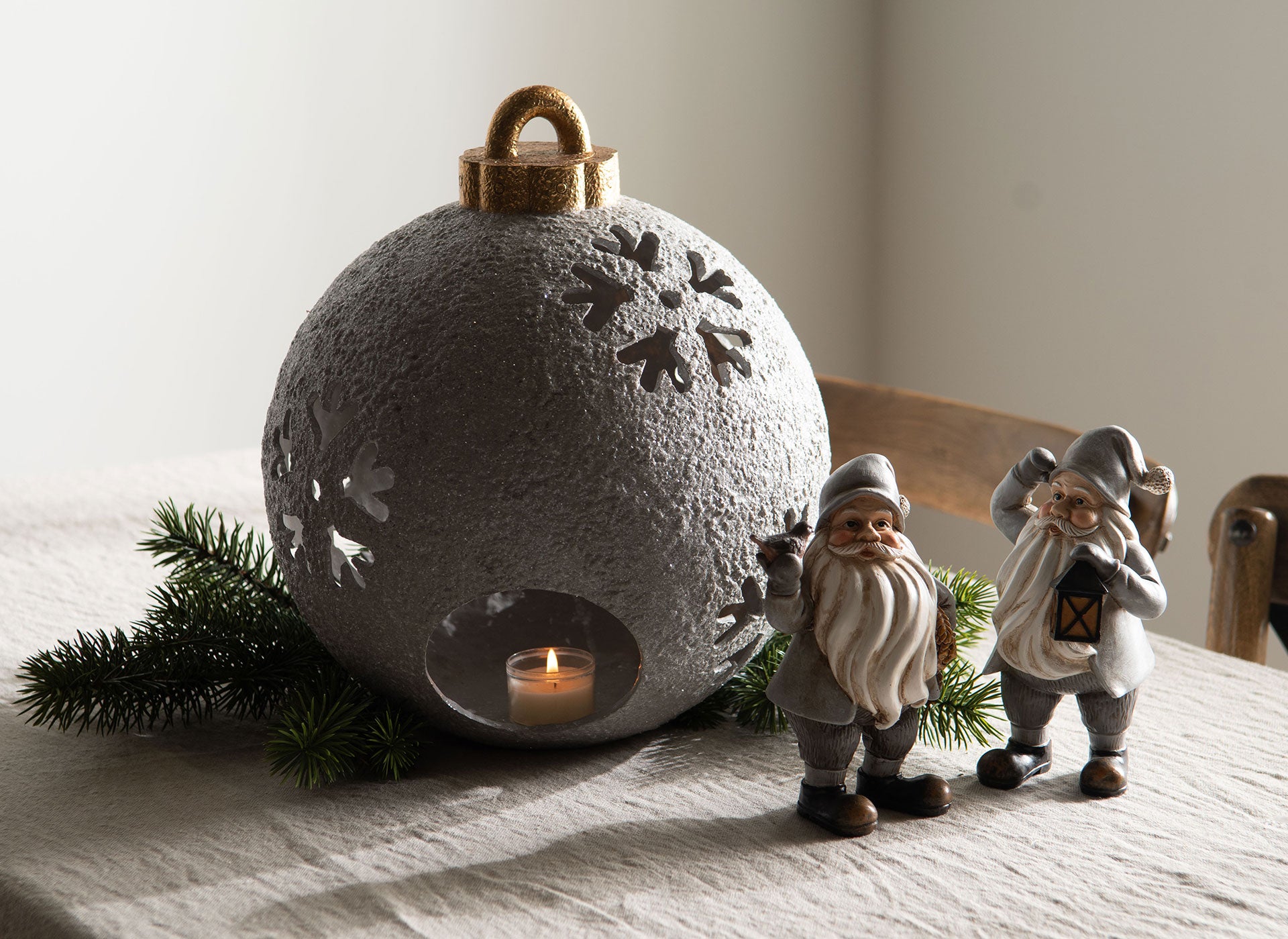 Grå värmeljuslykta med snöflingsmönster, guldhandtag och tänd ljus inuti, omgiven av julnissar och granris | A Lot Decoration | Lilla Hem
