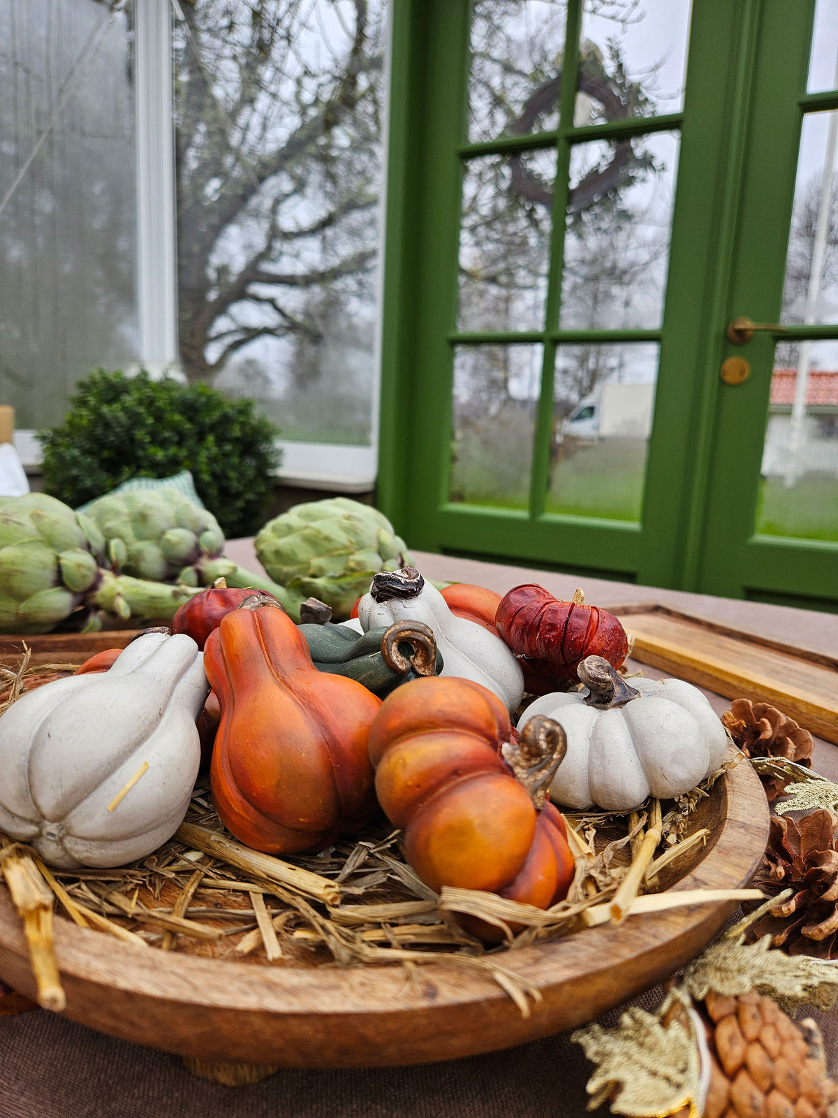 Närbild av dekorativa minipumpor i vit, orange och röd färg arrangerade på trä framför gröna fönster | A Lot Decoration | Lilla Hem