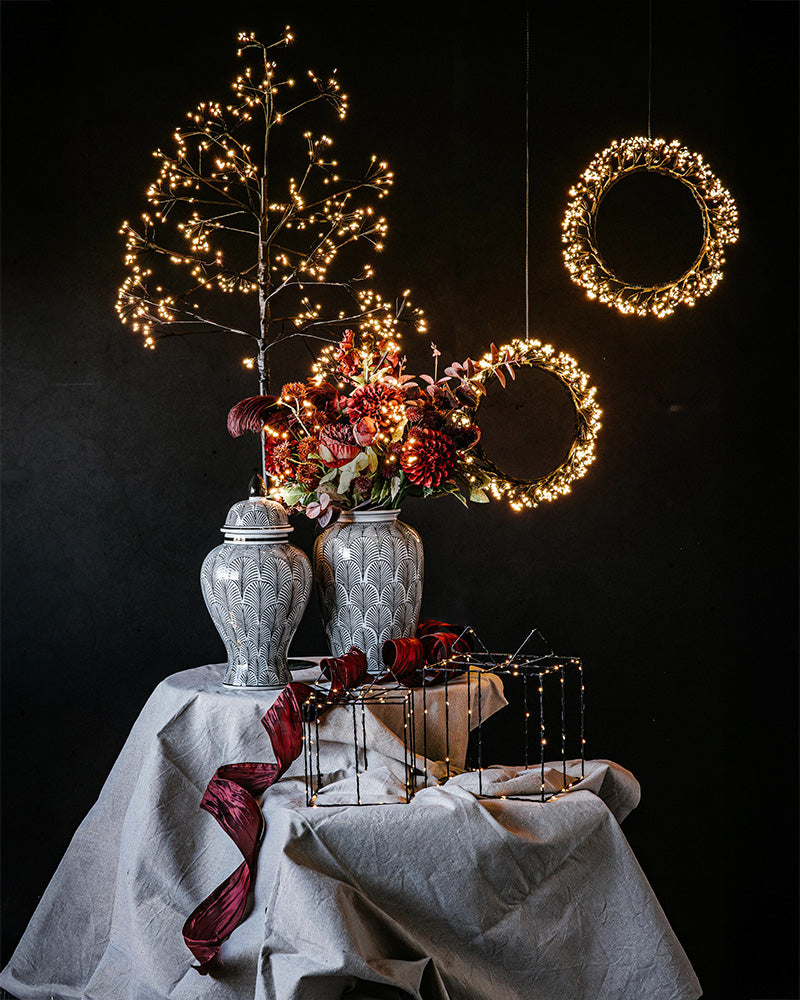 Dekorativ urna med fjädermönster, omgiven av julblommor och lysande ljusdekorationer mot mörk bakgrund | A Lot Decoration | Lilla Hem