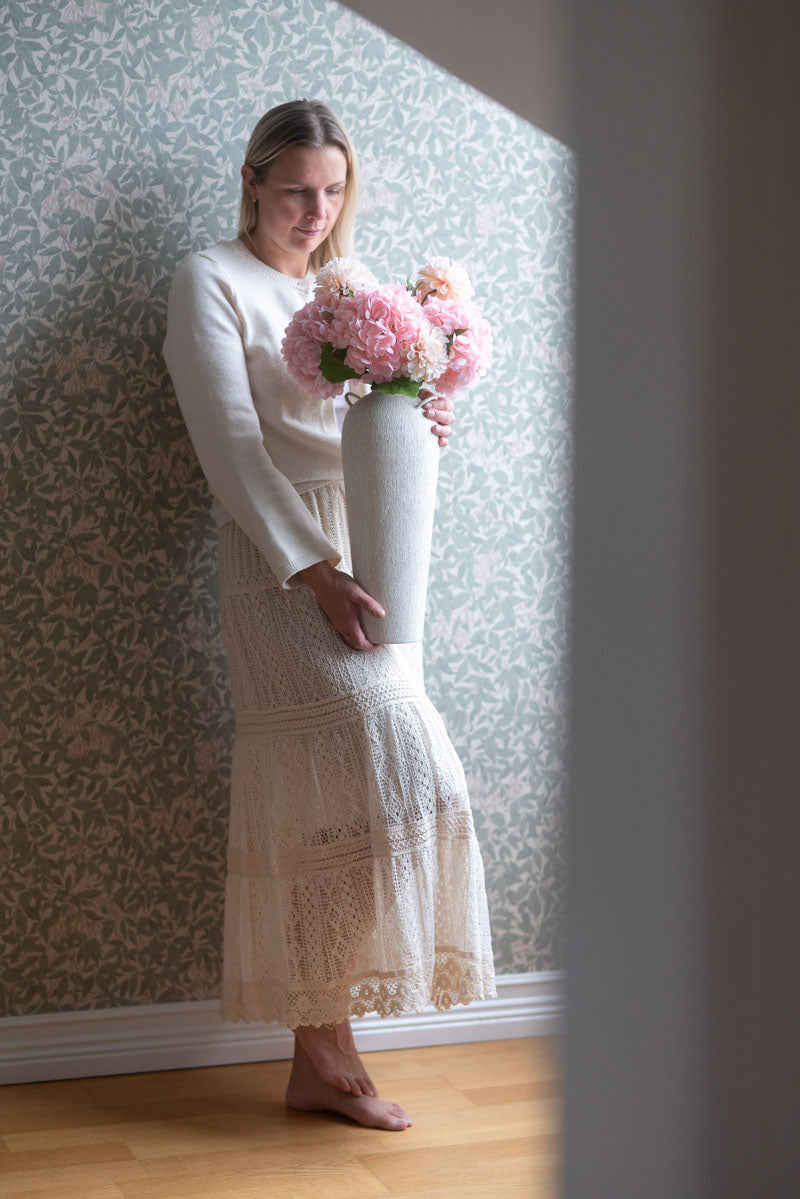 Modell bär vit långärmad tröja och spetsig kjol, håller vas med rosa blommor | A Lot Decoration | Lilla Hem