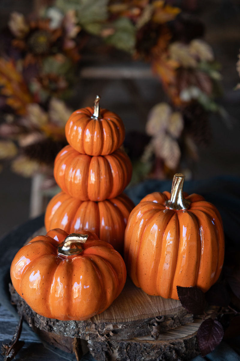 Tre glansiga orange pumpor i olika storlekar på trästamme med höstlöv i bakgrunden | A Lot Decoration | Lilla Hem