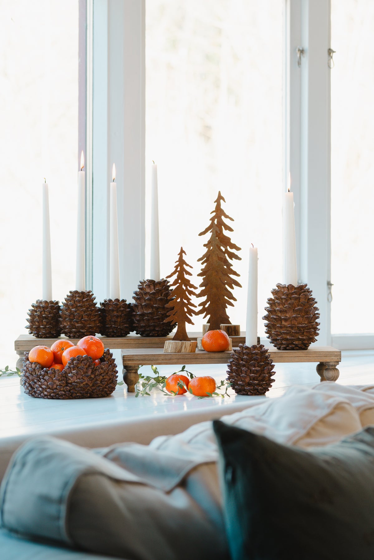 Ljusstake i form av tallkottar med brinnande ljus, dekorerad med små orangefärgade fruktdekorationer och träfigurer | A Lot Decoration | Lilla Hem