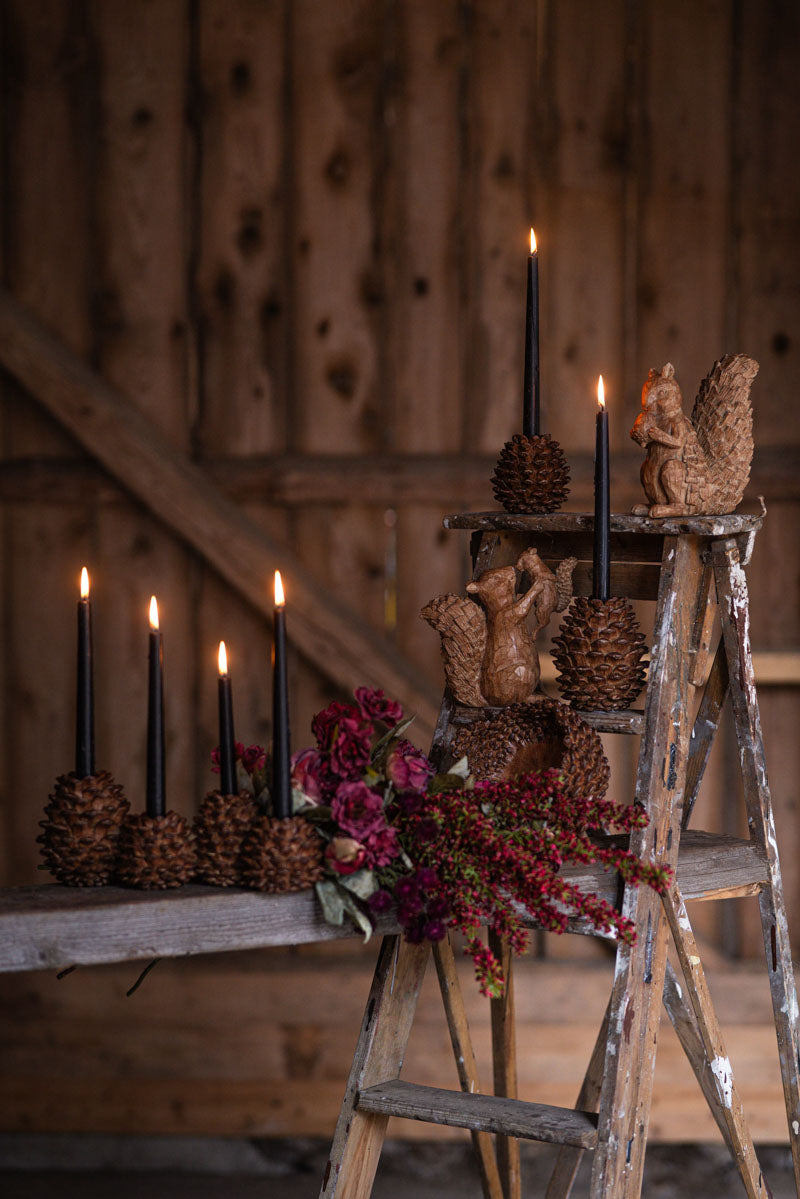 Ljusstake av tallkottar med brinnande svarta ljus, dekorerad med träfigurer och röda blommor | A Lot Decoration | Lilla Hem