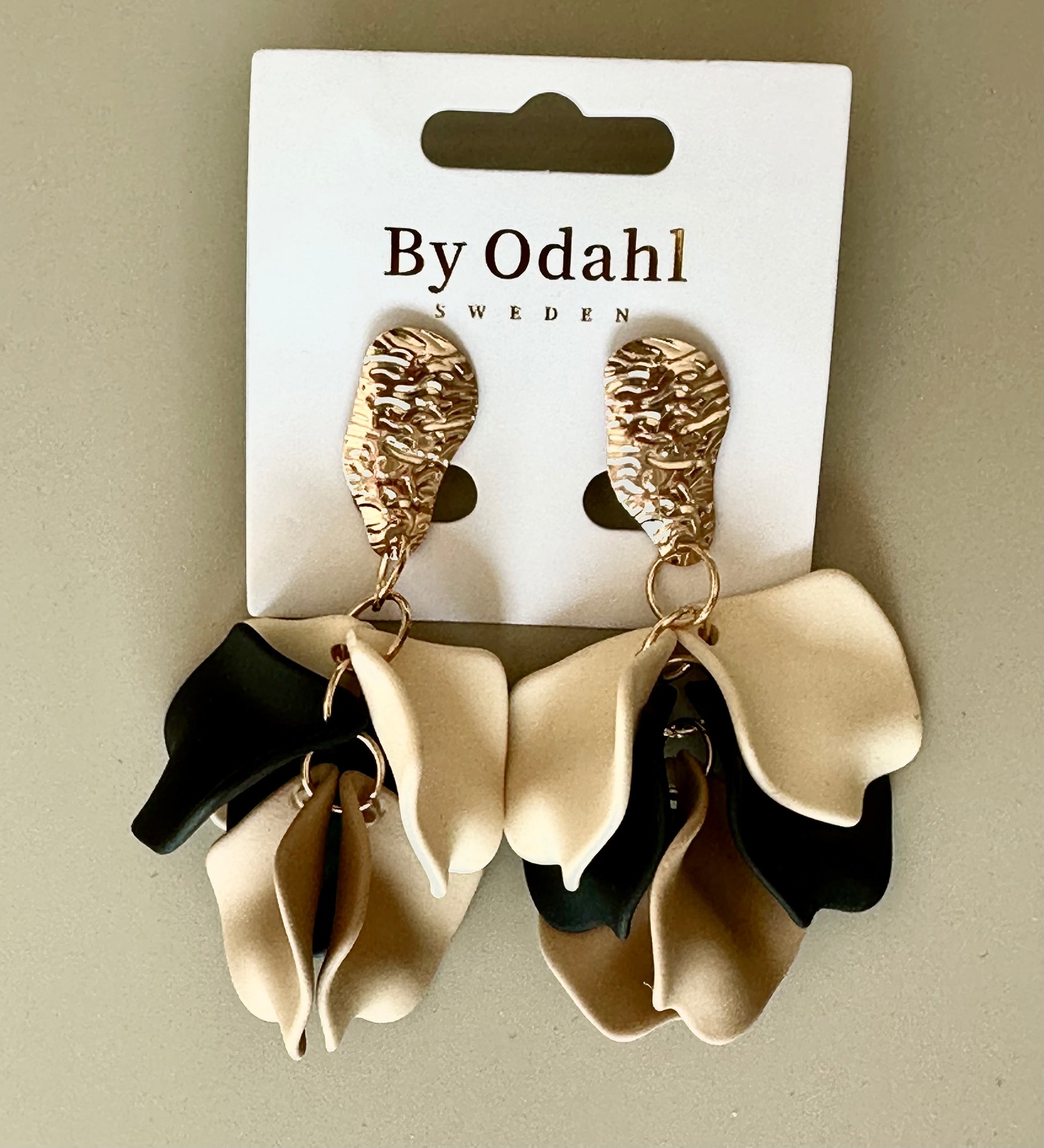 Örhängen med strukturerad guldtopp och voluminösa svart-beige-cream rosettdetaljer på förpackning | By Odahl Sweden | Lilla Hem