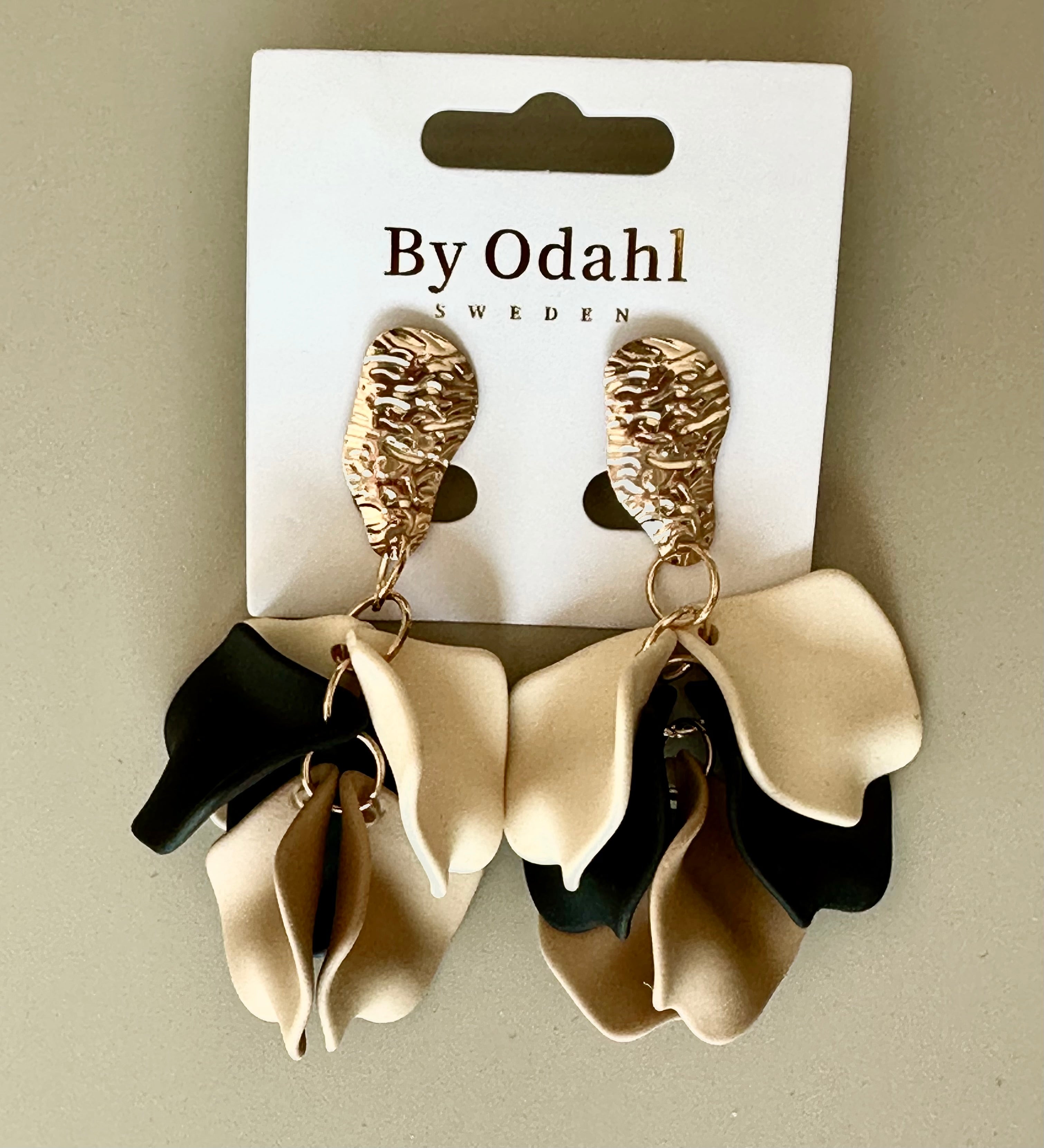 Örhängen med strukturerad guldtopp och voluminösa svart-beige-cream rosettdetaljer på förpackning | By Odahl Sweden | Lilla Hem