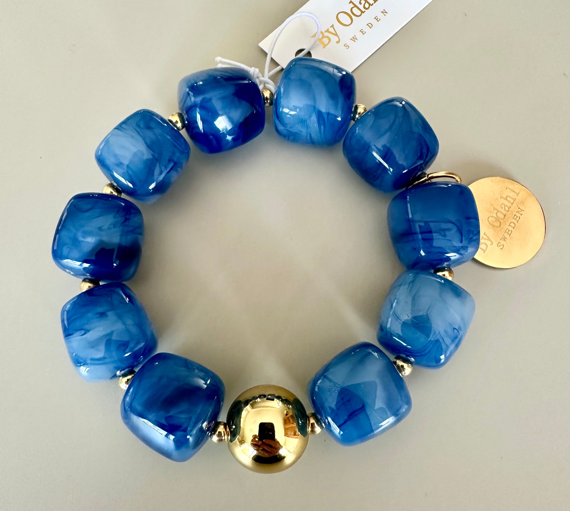 Armband med nio blå glansiga pärlor och guldtonade metalldetaljer, fotograferat ovanifrån mot neutral bakgrund | By Odahl Sweden | Lilla Hem