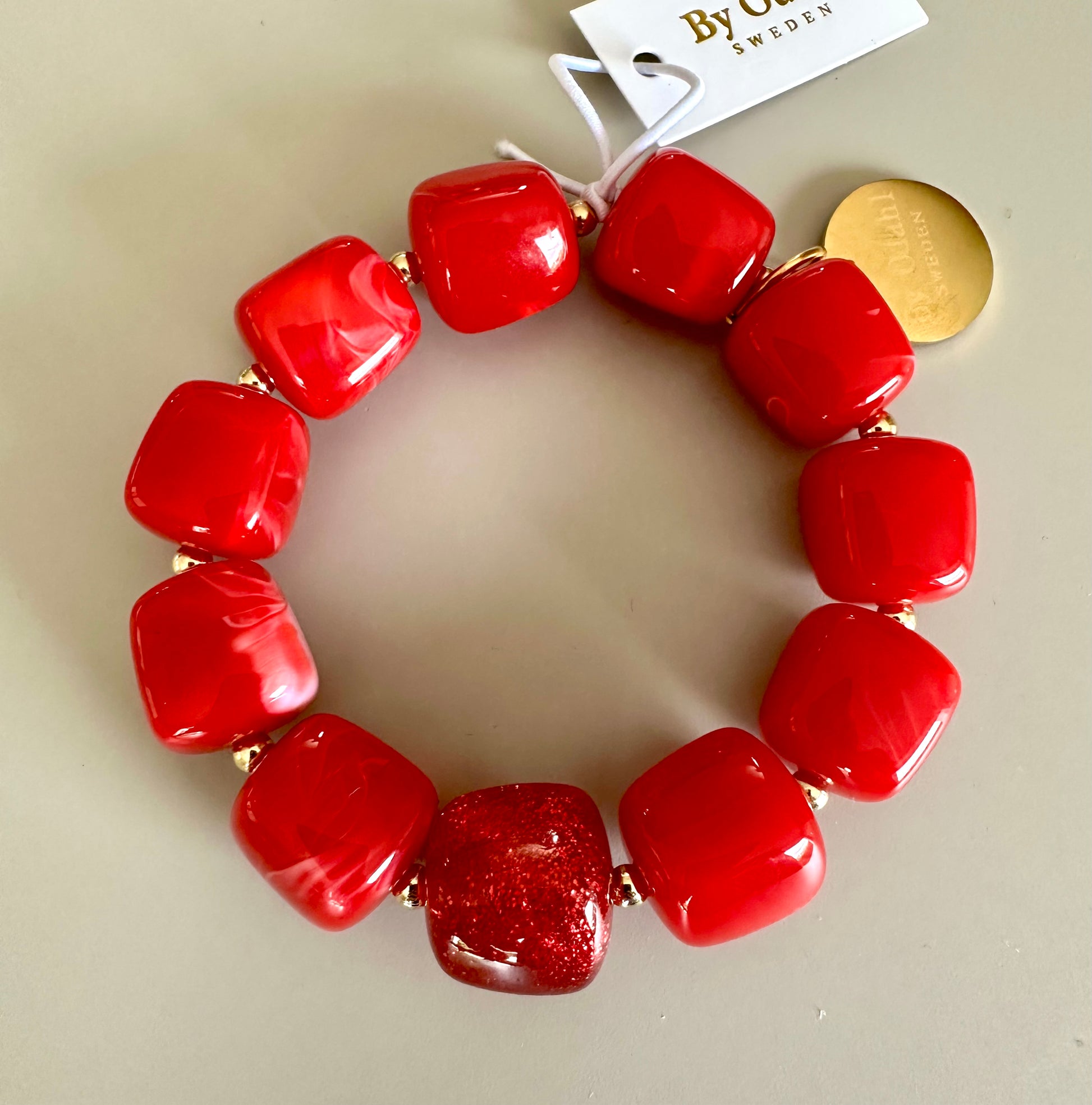 Armband med röda glansiga pärlor och en guldpläterad detalj, sett från ovan mot neutral bakgrund | By Odahl Sweden | Lilla Hem