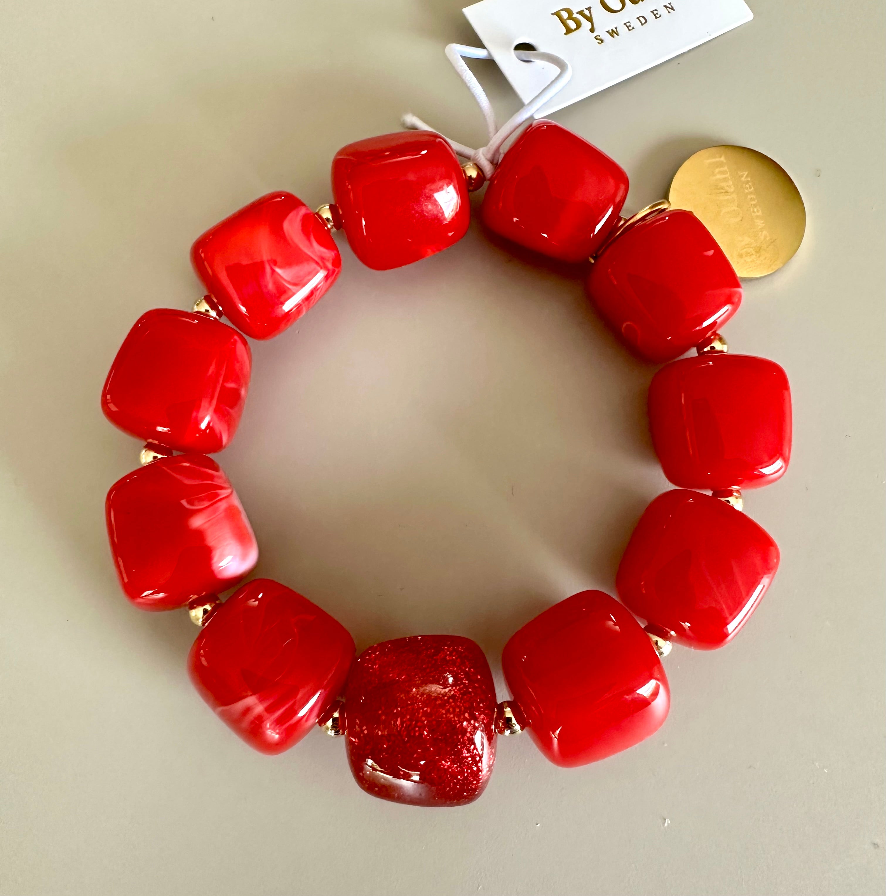 Armband med röda glansiga pärlor och en guldpläterad detalj, sett från ovan mot neutral bakgrund | By Odahl Sweden | Lilla Hem