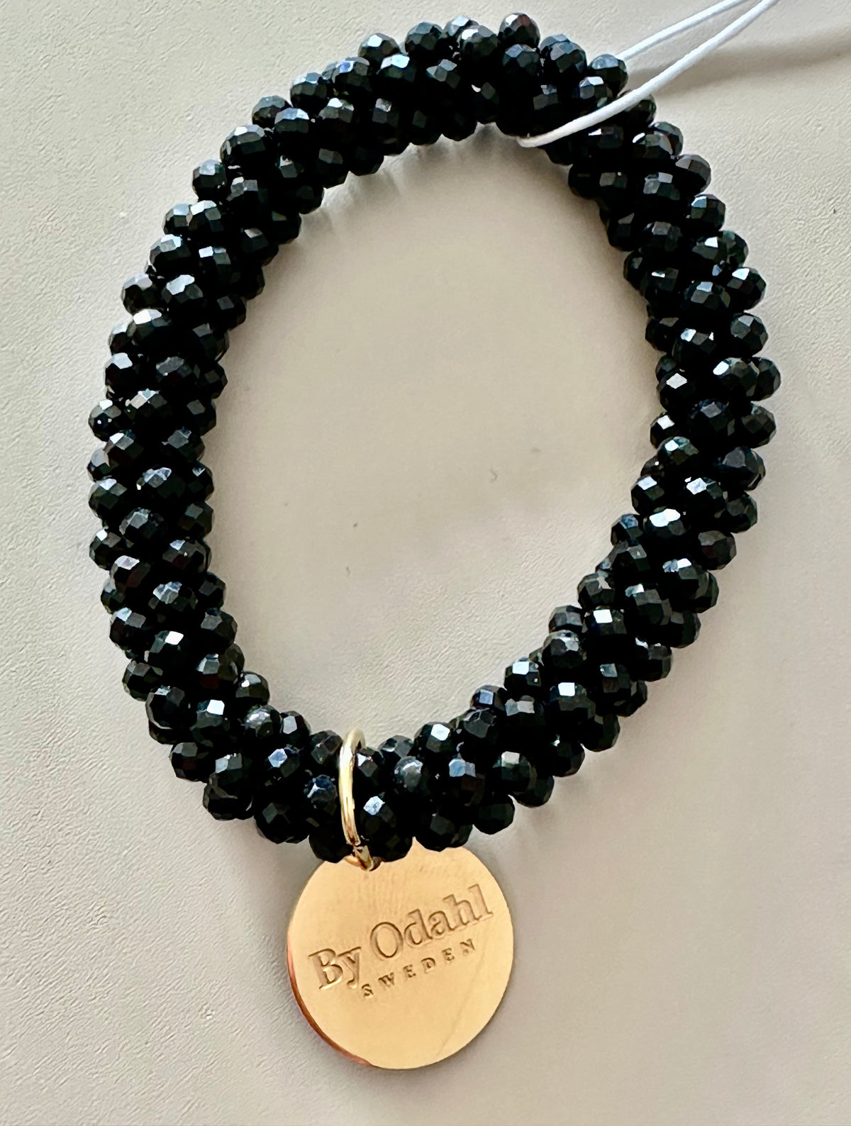 Närbild av armband med svarta fasetterade pärlor och guldpläterad bricka med text | By Odahl Sweden | Lilla Hem
