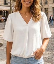 Modell bär vit blus med ballongärmar och v-ringning, fotograferad framifrån utomhus | Caramelle Fashion | Lilla Hem