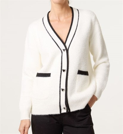 Modell bär vit cardigan med svart trim och hjärtknappar, sedd framifrån | Caramelle Fashion | Lilla Hem