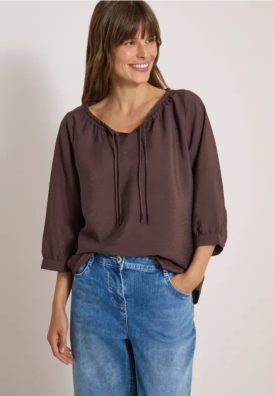Modell bär brunviolett blus med snörhals och puffärmar tillsammans med blå jeans, framifrån | Cecil | Lilla Hem