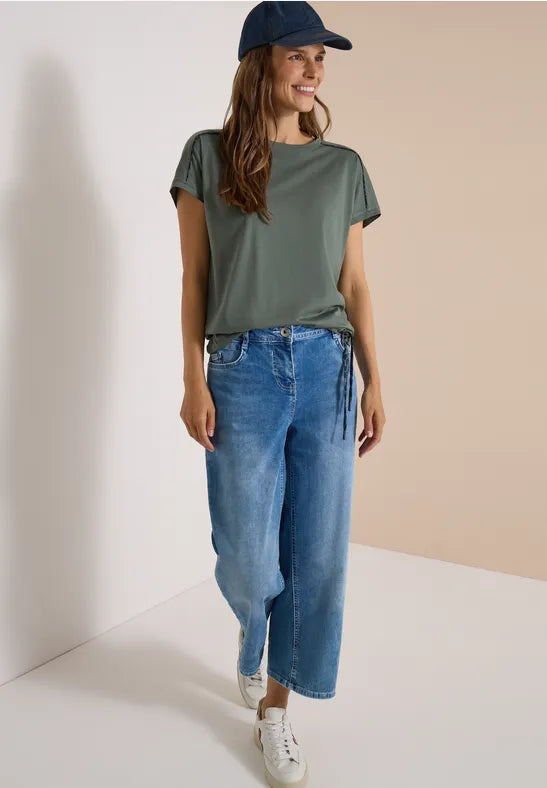 Modell bär grågrön t-shirt med vida jeansbyxor, sett framifrån i helkroppsvy | Cecil | Lilla Hem