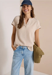 Modell bär beige kortärmad blus med v-ringning och ljusblå jeans, sett framifrån | Cecil | Lilla Hem