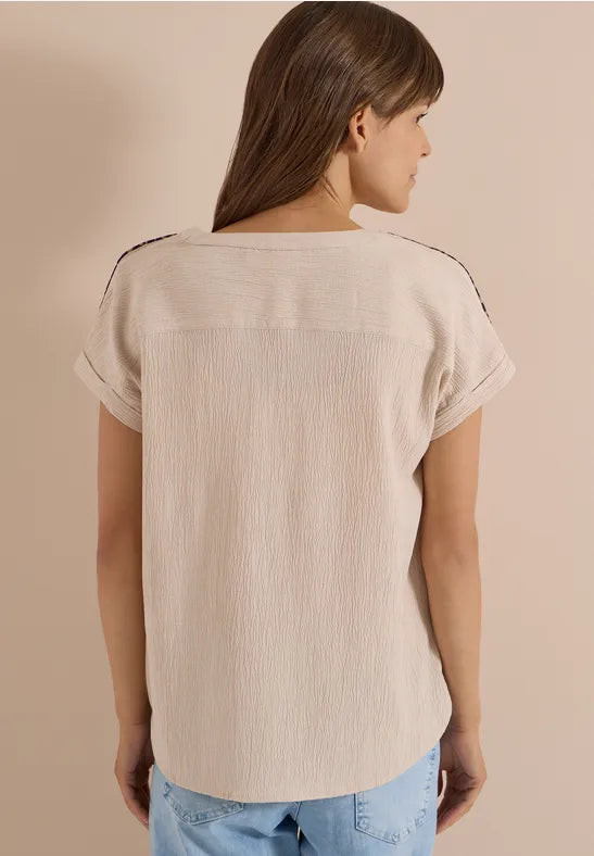 Modell bär beige blus sett bakifrån, visar texturerad bomullsstoff och kort volangärm | Cecil | Lilla Hem