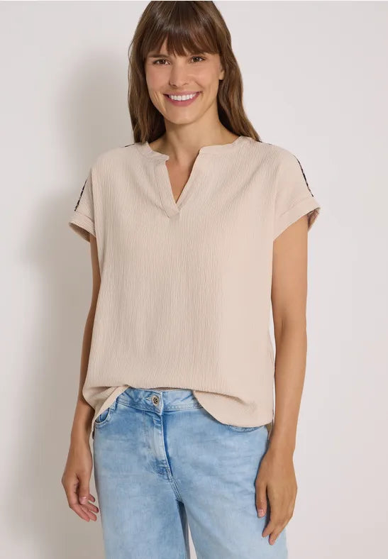 Modell bär beige blus med v-ringning och korta ärmar, kombinerad med ljusblå jeans | Cecil | Lilla Hem