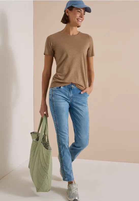 Modell bär beige t-shirt och ljusblå straight jeans, hålls framifrån med grön väska | Cecil | Lilla Hem