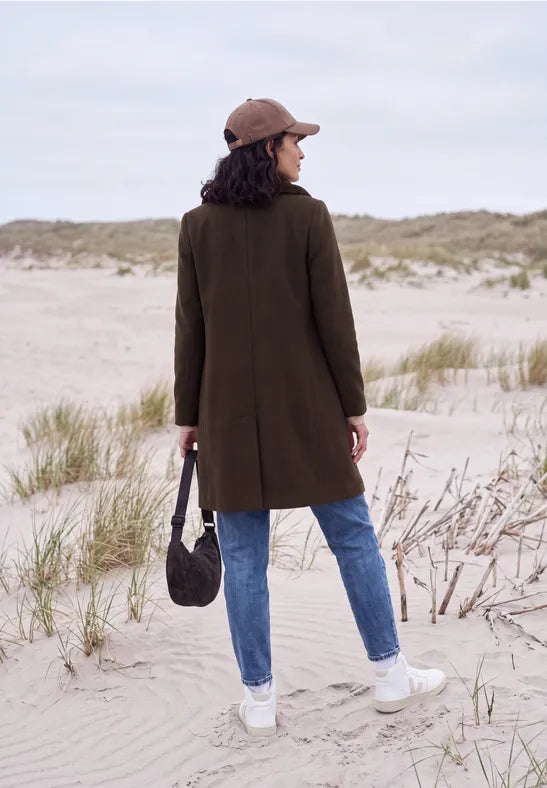 Modell bär olivgrön kappa sedd bakifrån på strand med keps och väska | Cecil | Lilla Hem