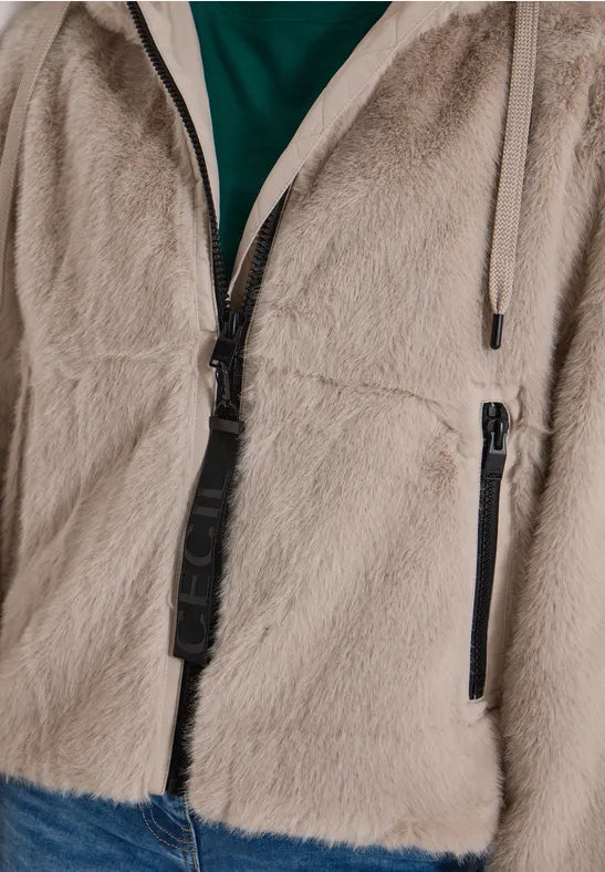 Närbild av beige fluffig jacka med svarta dragkedjor och grön tröja synlig under | Cecil | Lilla Hem