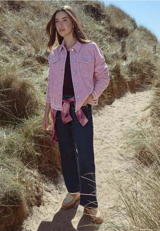 Modell bär rosa jeansjacka med fickor och knappar, svarta jeans och rosa halsduk på sandstrand | Cecil | Lilla Hem