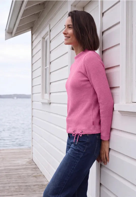 Modell bär rosa ribbad tröja sett från sidan mot vit husfasad | Cecil | Lilla Hem