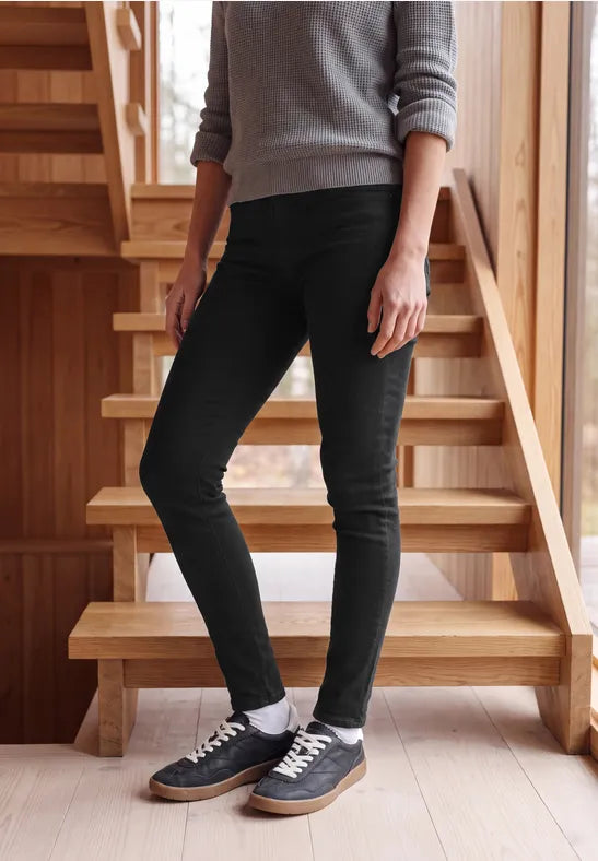 Modell bär svarta stretchiga jeans med grå ribbad tröja, fotograferad framifrån på trappa | Cecil | Lilla Hem