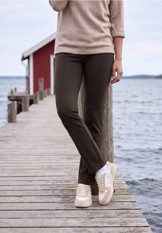 Modell bär bootcut-byxor i mörkbrun färg med beige sweatshirt, fotograferad från midjan ned på brygga | Cecil | Lilla Hem