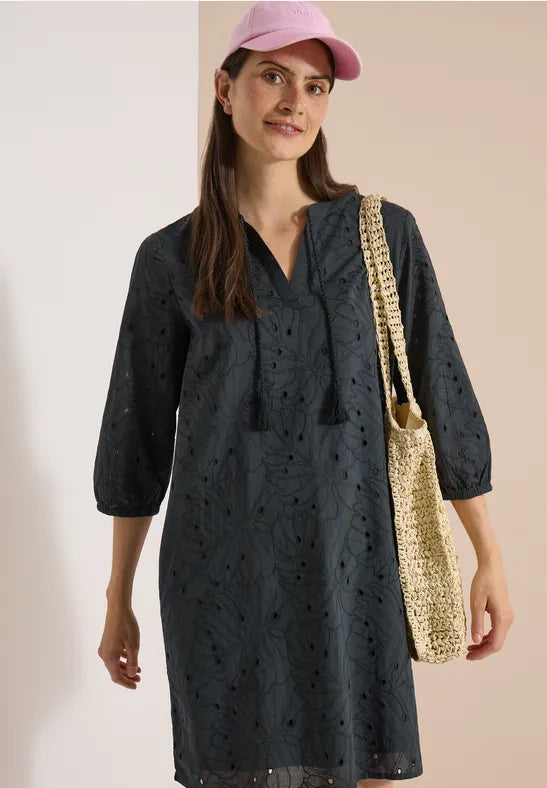 Modell bär marinblå broderad klänning framifrån med rosa keps och beige axelväska | Cecil | Lilla Hem