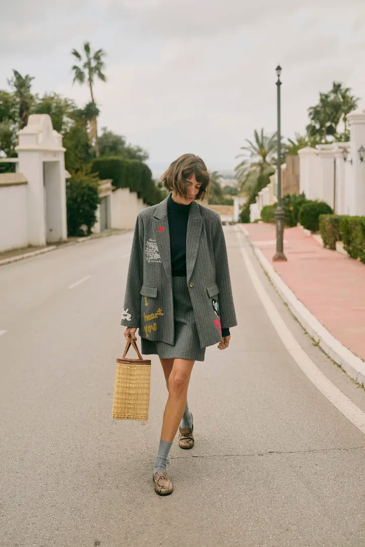 Modell bär grå oversized blazer med grafiska tryck, kombinerad med kort kjol, framifrån på gata | CULTURE | Lilla Hem