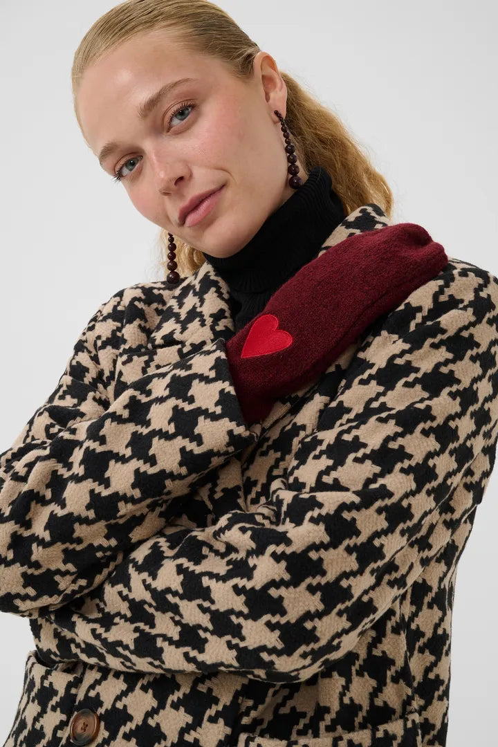 Modell bär burgundy handskar med rött hjärta, visas från sidan tillsammans med houndstooth-mönstrad jacka | CULTURE | Lilla Hem
