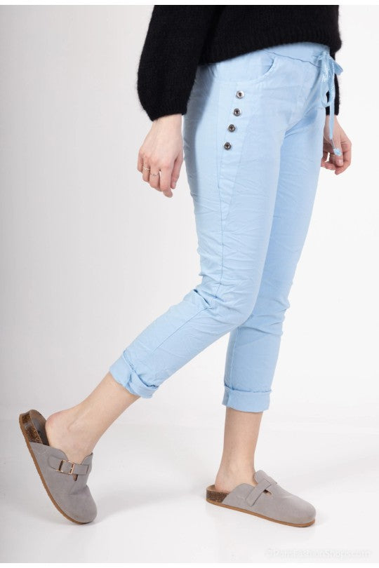 Modell bär ljusblå capri-jeans med upprullade ben och dekorativa knappar sett från sidan | Miss Azur | Lilla Hem