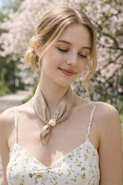 Modell bär beige scarf med pärla omkring halsen, sett från sidan mot blomstrande bakgrund | BEST ANGEL | Lilla Hem