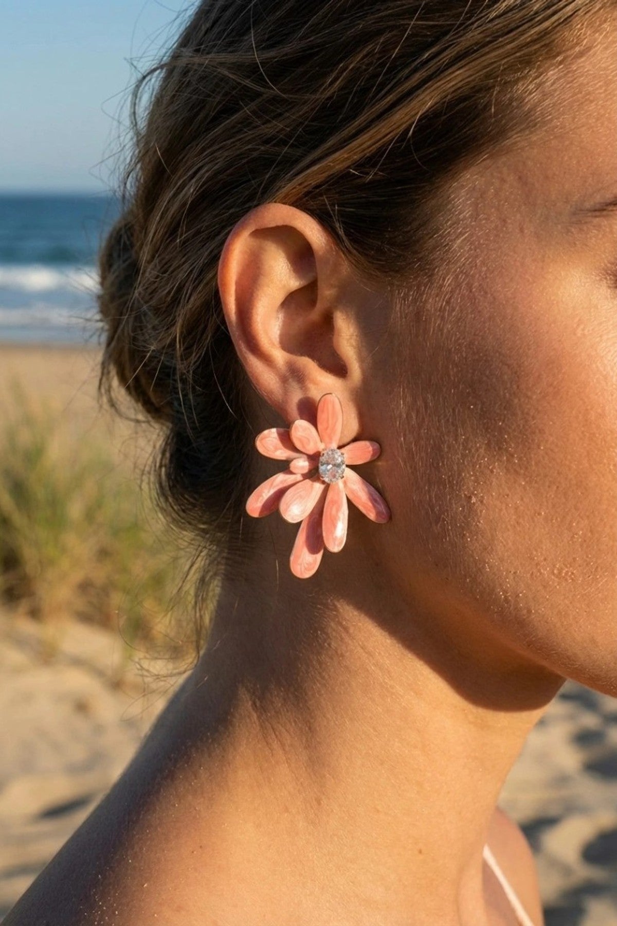 Närbild av örhänge i blomsterform med rosa kronblad och strass i mitten, bärat vid stranden | Beli & Jolie | Lilla Hem