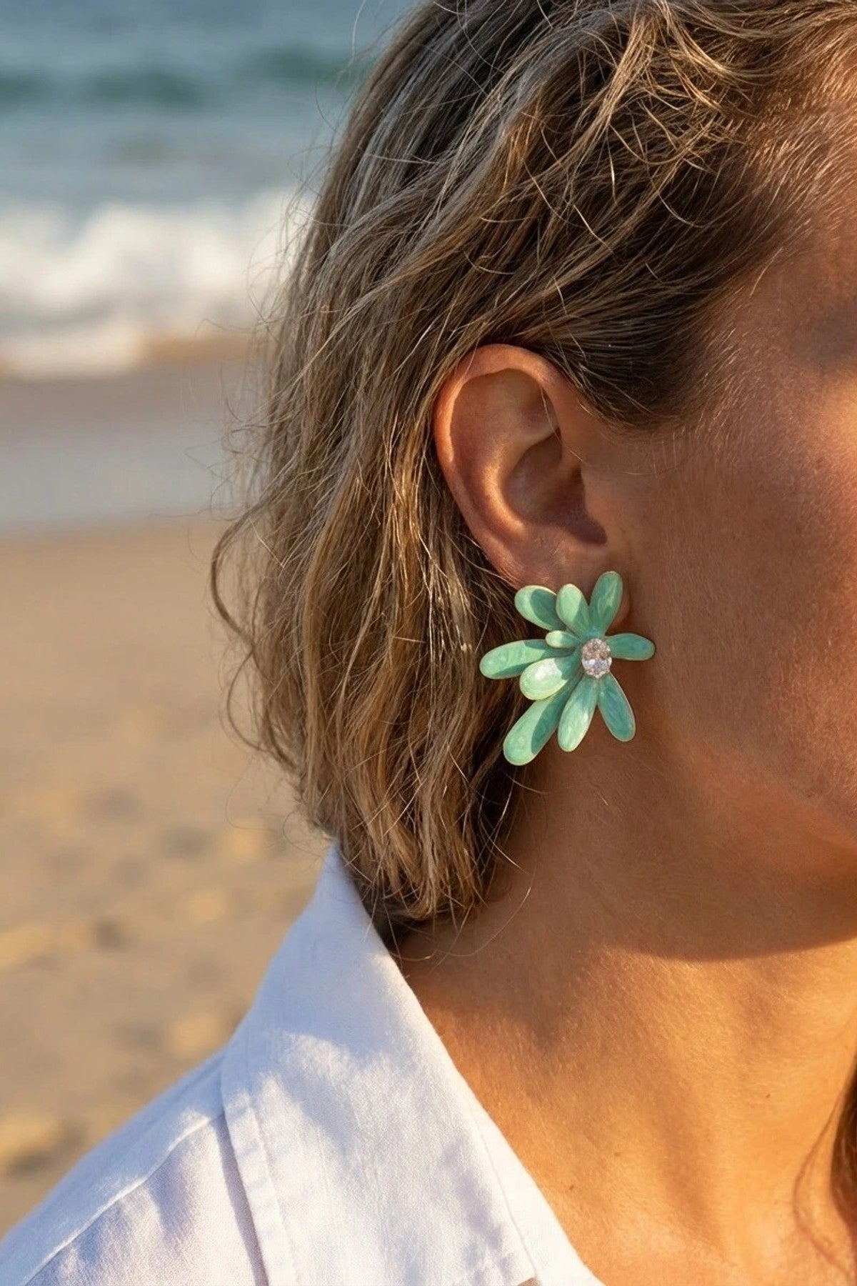 Närbild av grön blomsterörhänge med strass i mitten, bärat på modell vid strand | Beli & Jolie | Lilla Hem