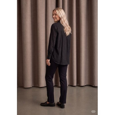 Modell bär svart skjorta och mörka jeans, fotograferad från sidan mot beige gardinbakgrund | I SAY | Lilla Hem