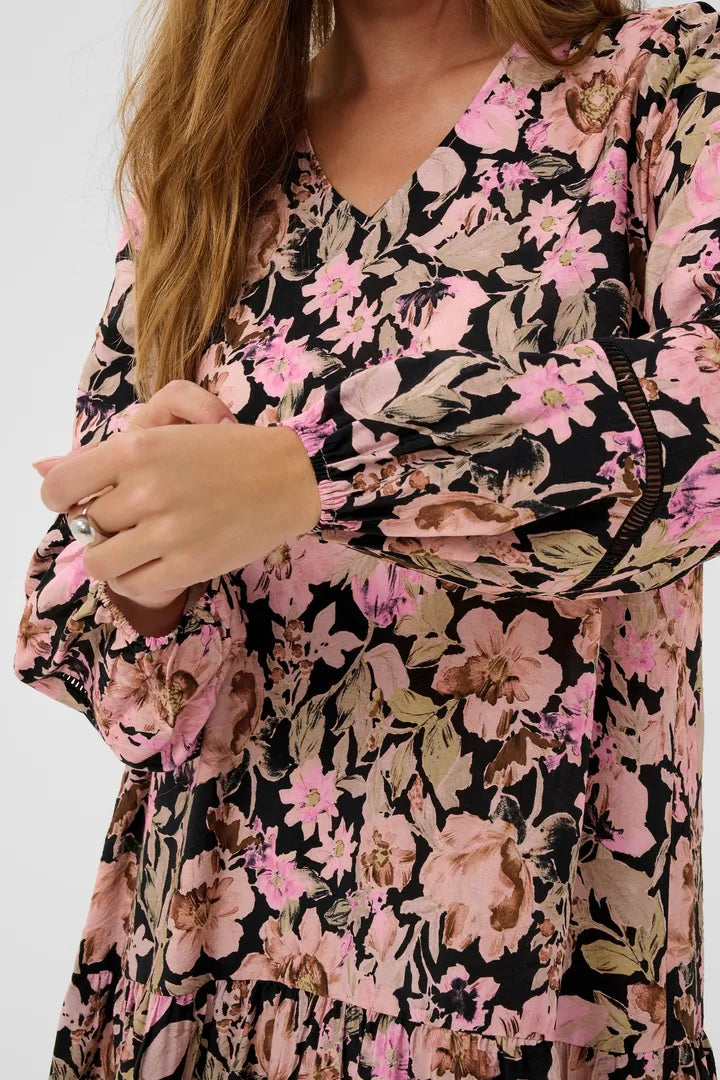 Modell bär blommig klänning med rosa och beiga blommor på svart botten, sett framifrån | KAFFE | Lilla Hem