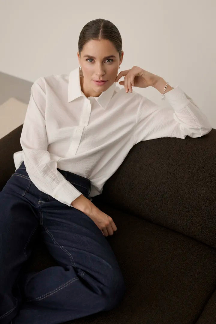 Modell bär vit skjorta med klassisk krage och marinblå jeans, sittande framifrån | KAFFE | Lilla Hem