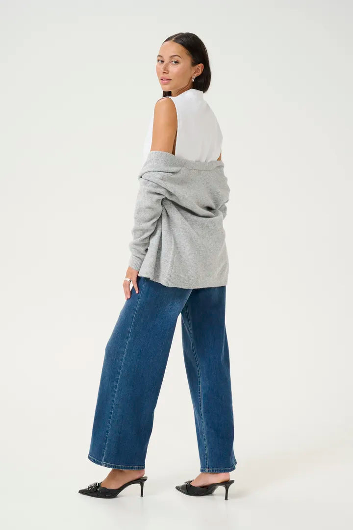 Modell bär grå stickad tröja med bardotöverslag, vit linne och blå jeans, fotograferad från sidan bakåt | KAFFE | Lilla Hem