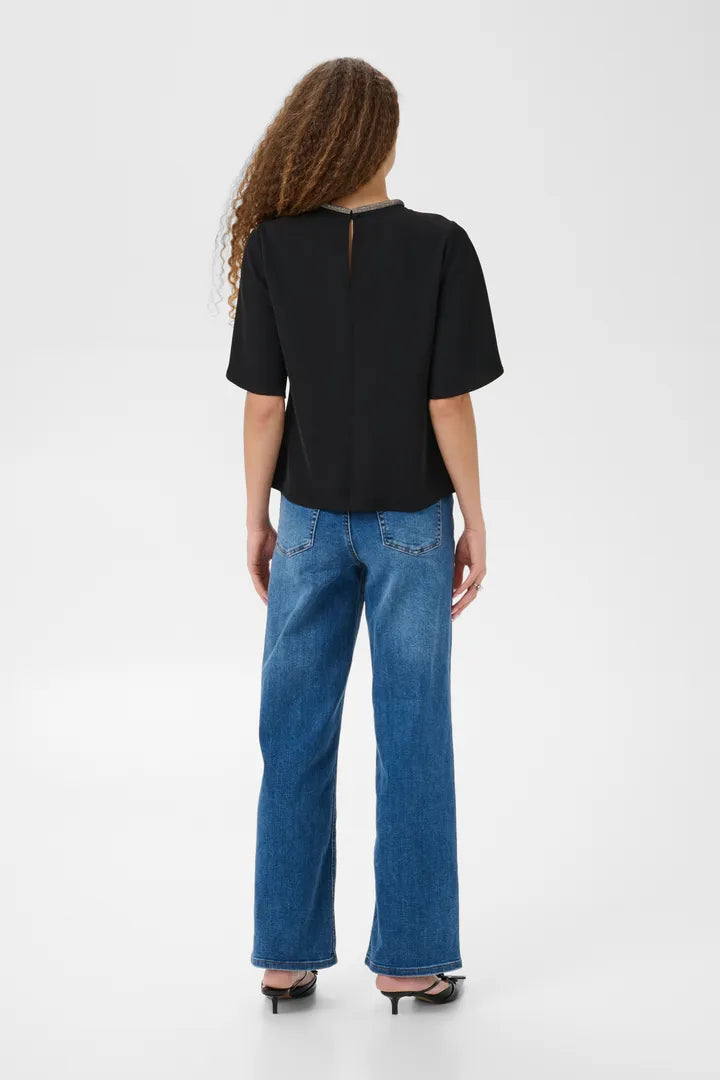 Modell bär svart blus med kort ärm sedd bakifrån tillsammans med blå jeans | KAFFE | Lilla Hem