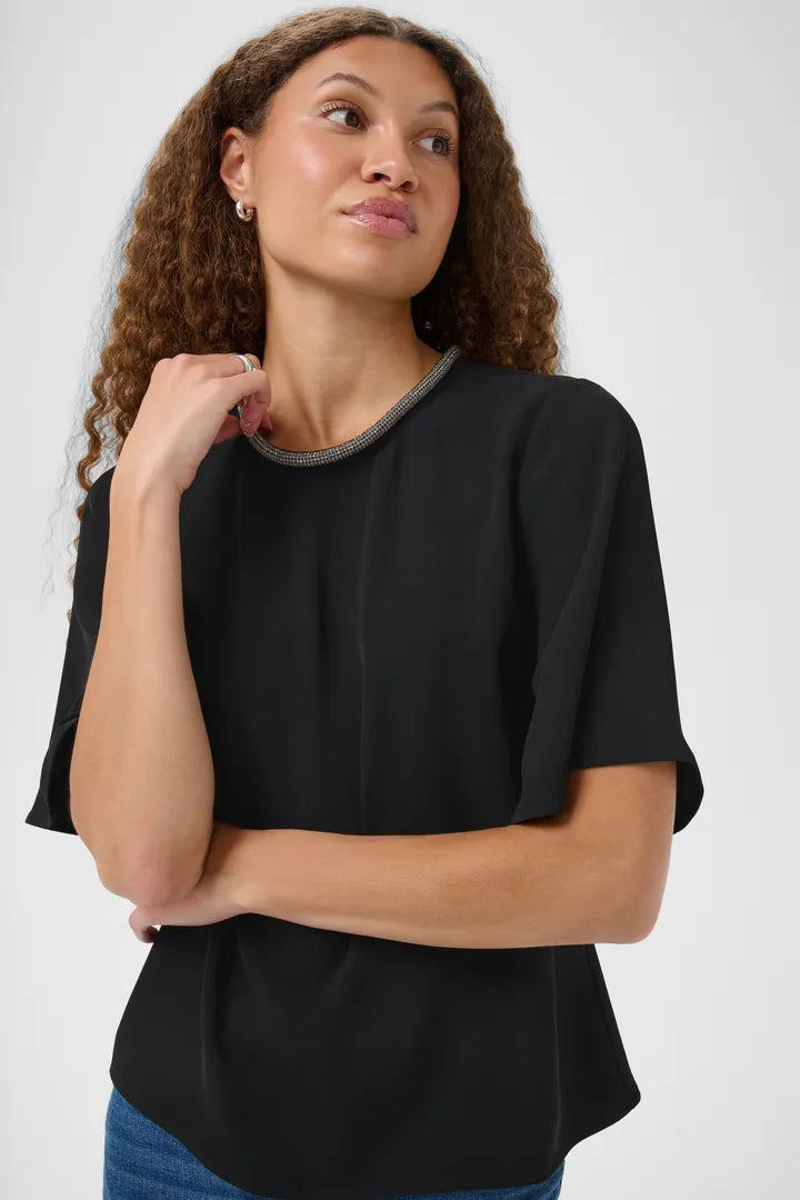 Modell bär svart blus framifrån med dekorativ halsband och kortärmad snitt | KAFFE | Lilla Hem
