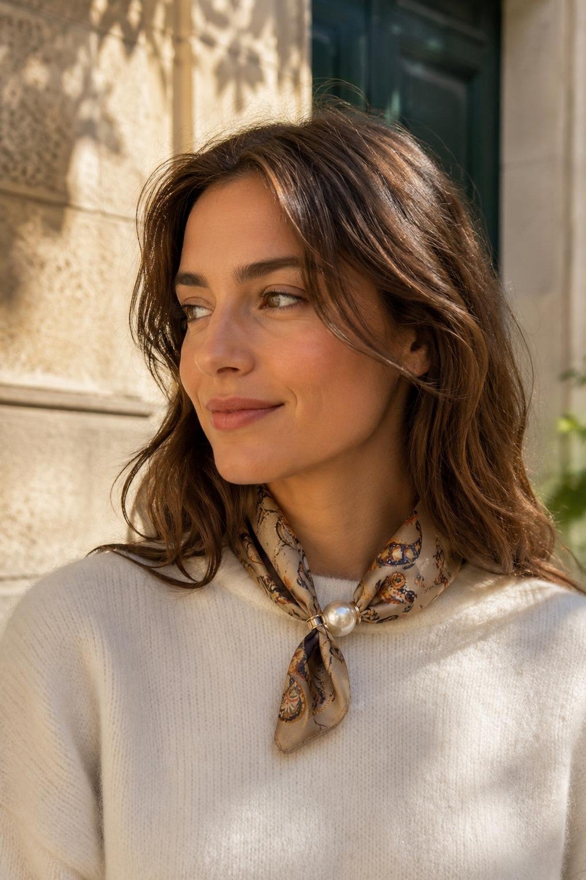 Modell bär beige scarf med mönster och pärldetalj, sett från sidan mot stenmur | BEST ANGEL | Lilla Hem