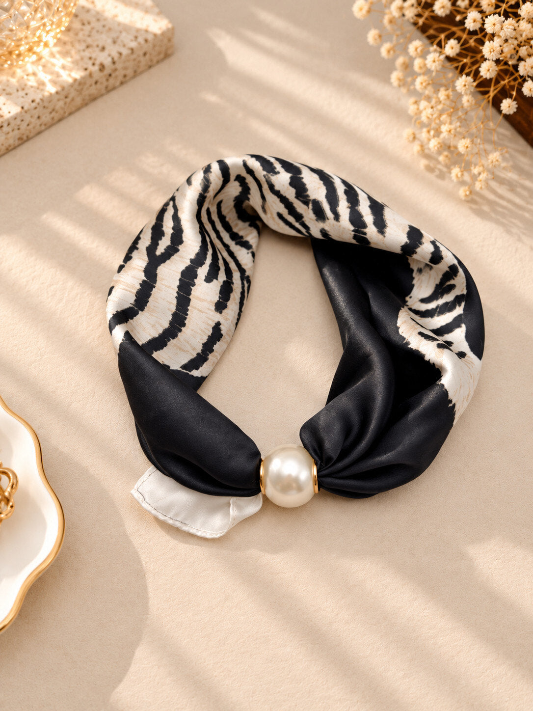 Scarf med zebramönster i svart och vitt, dekorerad med pärlkula, liggande platt på beige underlag | CLAREN B | Lilla Hem