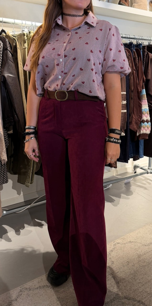 Modell bär vinröd mockaimitation-byxa med bälte, kombinerad med randig rosa skjorta, framifrån | Caramelle Fashion | Lilla Hem