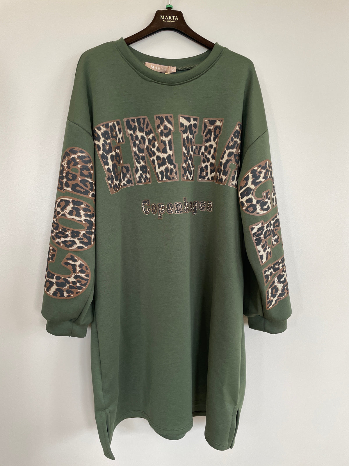 Grön sweatshirtklänning med leopardmönstrad text och armdetaljer, hängande på galge framifrån | MARTA du Chateau | Lilla Hem