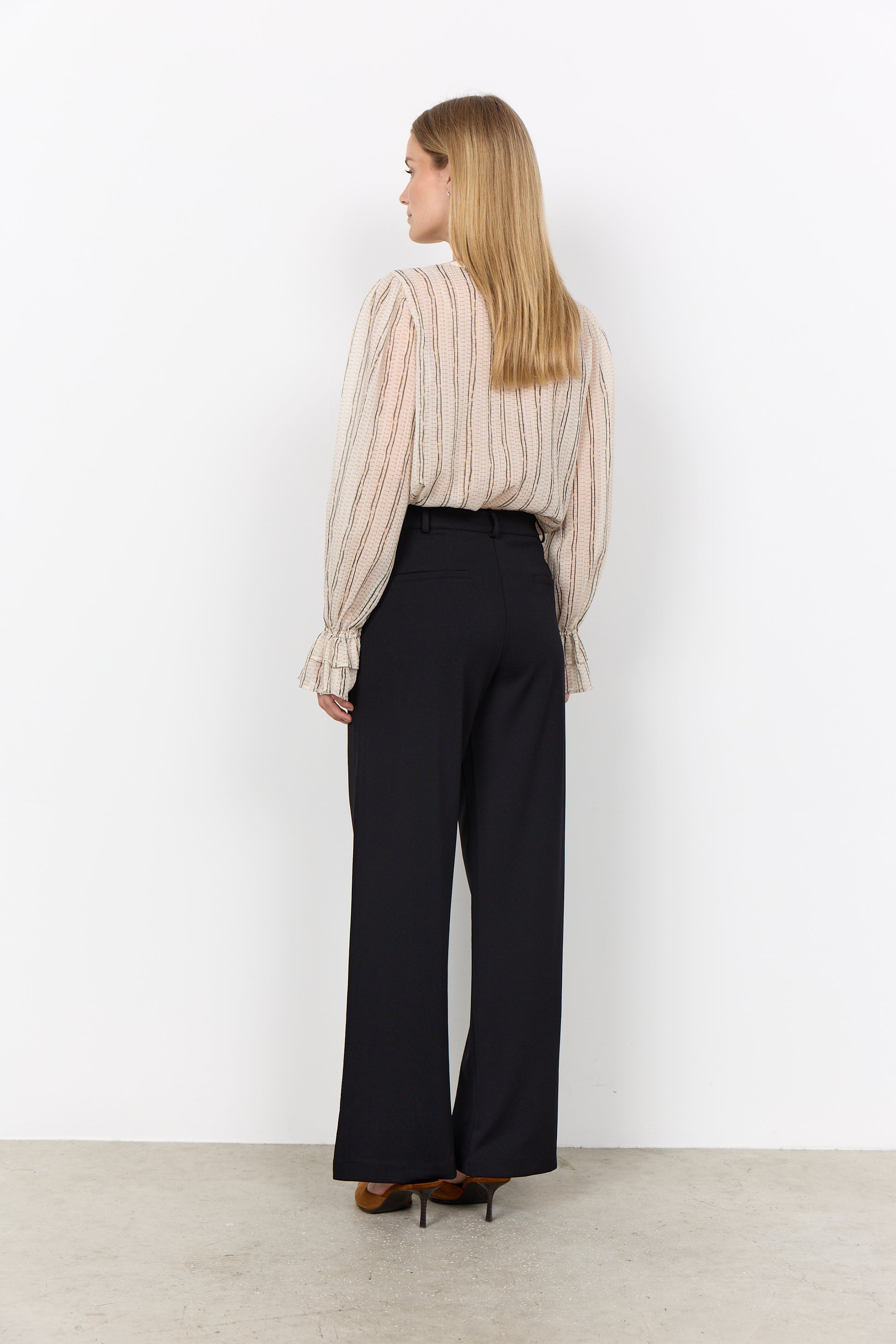 Modell ses bakifrån i randig beige blus med volangmanschetter och svarta vida byxor | Soya Concept | Lilla Hem