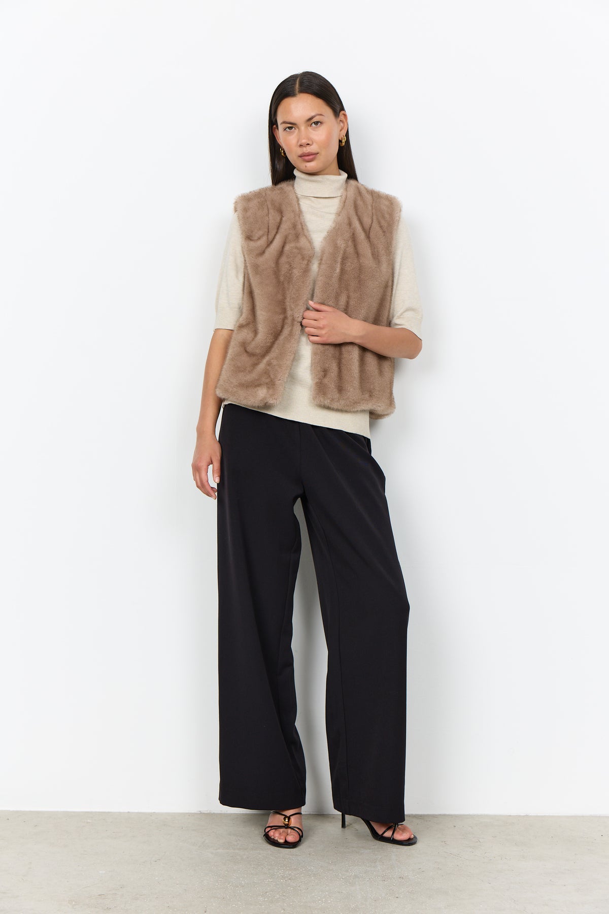 Modell bär beige pälsväst över vit polotröja och svarta byxor, framifrån | Soya Concept | Lilla Hem