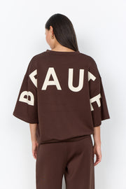 Modell bär brun t-shirt sedd bakifrån med stort vitt tryck på ryggen | Soya Concept | Lilla Hem