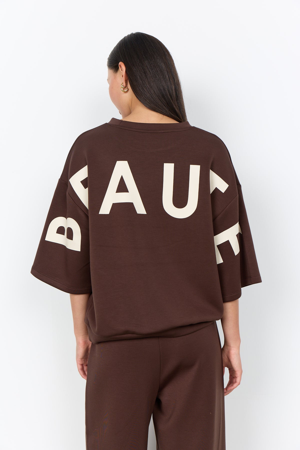 Modell bär brun t-shirt sedd bakifrån med stort vitt tryck på ryggen | Soya Concept | Lilla Hem
