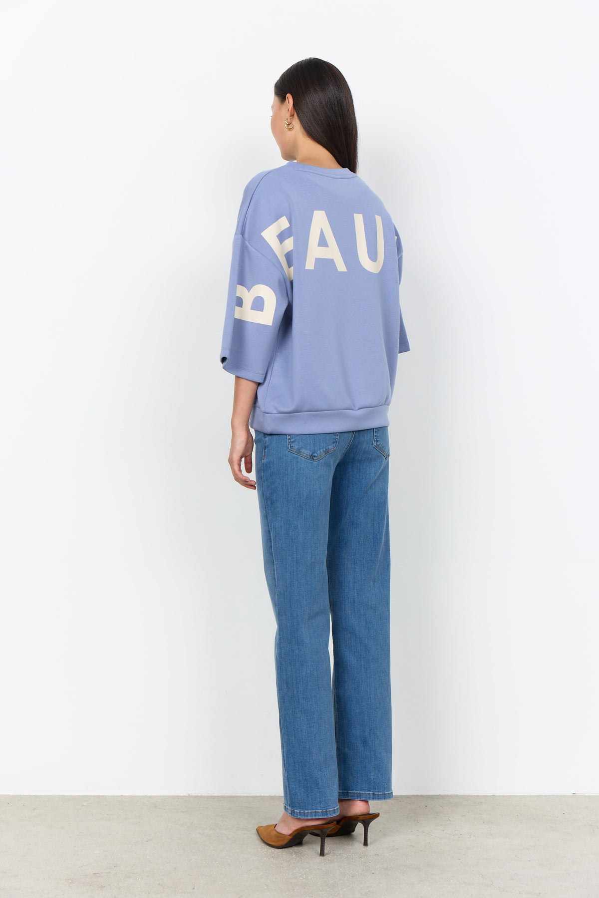 Modell bär lila sweatshirt med vit textprint bakifrån tillsammans med blå jeans | Soya Concept | Lilla Hem