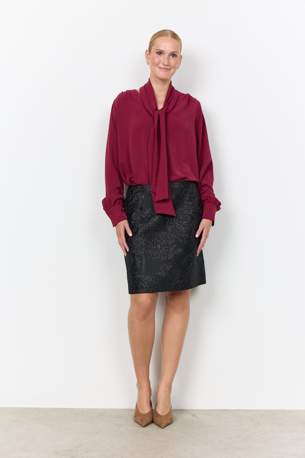 Modell bär vinröd blus med draperingskrage tillsammans med svart mönstrad kjol, sett framifrån | Soya Concept | Lilla Hem